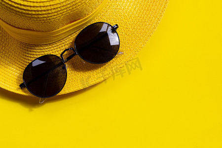 有黄色背景夏季帽子的太阳镜。