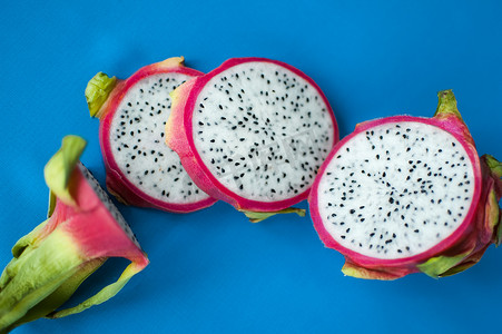 蓝色背景上带有粉红色皮肤和白色果肉的火龙果或火龙果片，带有黑色种子。