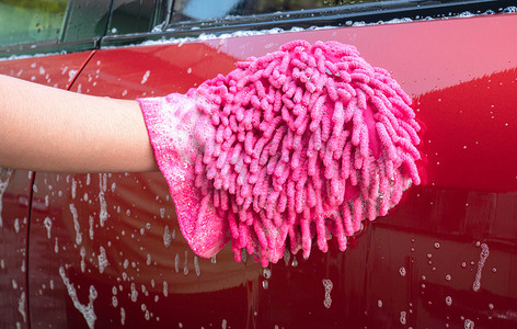 女手拿着带气泡的粉色手套，用于洗车。