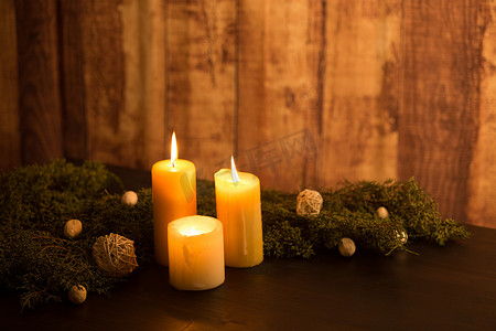 MInimal 圣诞节概念：深色木桌上的三根点燃的蜡烛和质朴的木质环境，配有松枝和白色自然装饰
