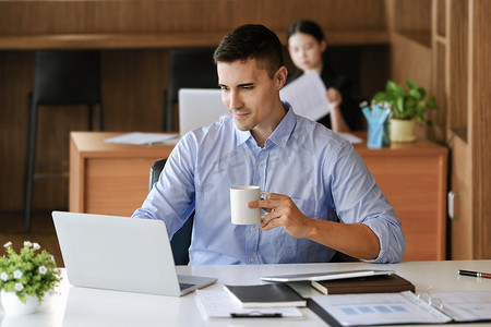 营销经理摄影照片_在使用电脑、iPad 和营销分析文件之前，男性营销经理一边工作一边喝咖啡以减少睡意。
