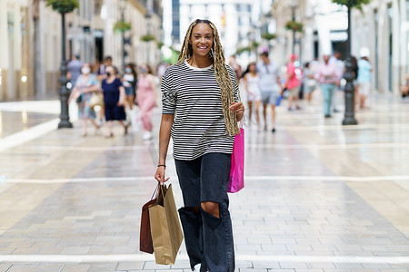 黑人女性，扎着彩色辫子，提着购物袋在街上。