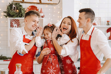 红色话剧摄影照片_一个幸福的家庭站在圣诞厨房里，互相涂抹面粉