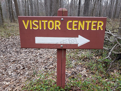 指向中心箭头摄影照片_棕色或红色游客中心标志，带有白色右箭头和森林中的树木