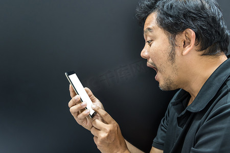 大吃一惊摄影照片_亚洲男子用深色风格的智能手机惊呆了