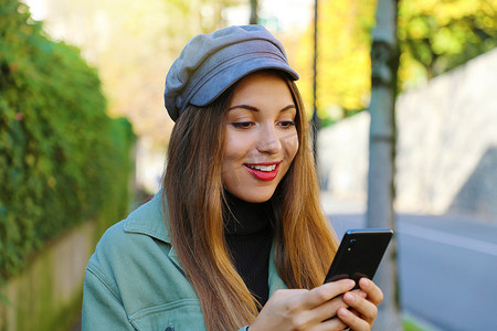 领用登记摄影照片_秋天户外，戴着帽子马球领和夹克的女人用手机发短信的特写。