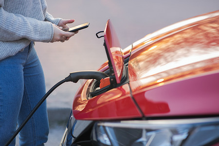 女人正在给电动汽车充电，以便在停车场给汽车电池充电。