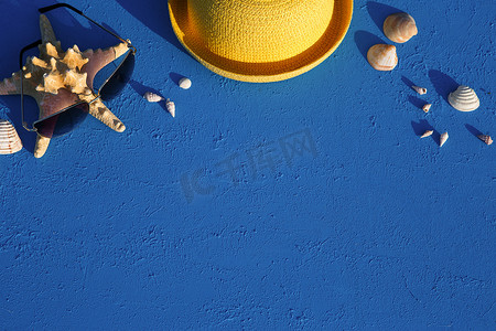 框架与航海主题的海滩配件：蓝色背景上的黄色草帽、太阳镜、海星和贝壳。