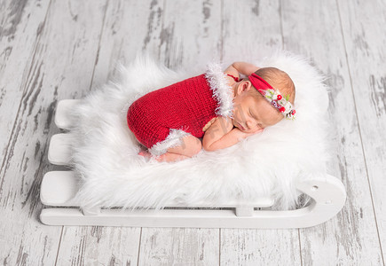 连衣裙子摄影照片_雪橇床上穿着红色连身衣的漂亮新生儿