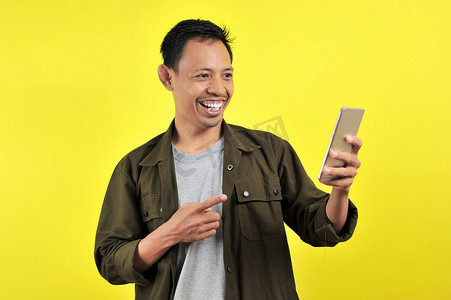 高兴摄影照片_年轻帅气的亚洲男子用智能手机微笑，很高兴