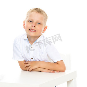 人坐在桌子前摄影照片_一个小男孩坐在桌子旁。