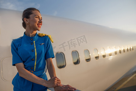 穿着蓝色制服的空姐在日落时站在户外微笑着站在户外。