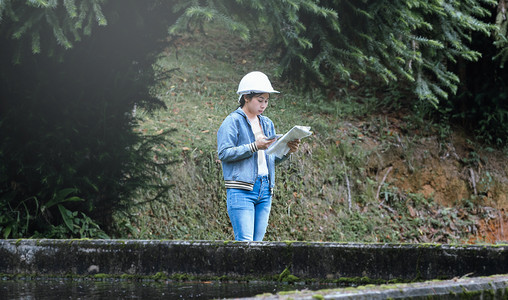 工厂污水摄影照片_在污水处理厂工作和控制水质的安全帽女生态学家。