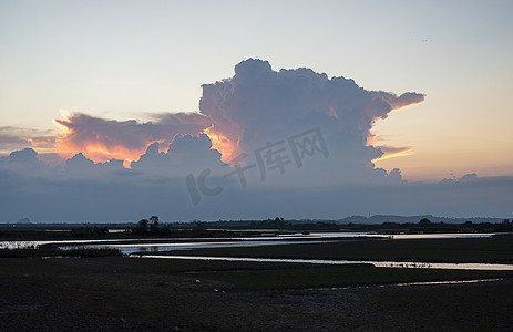 大海云朵背景摄影照片_傍晚的天空，蓝色的云朵撞击着太阳的橙色光芒，地面是沼泽