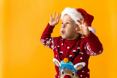 快乐微笑积极快乐积极学龄前小男孩的画像，戴着红色温暖的圣诞老人帽子，在橙色、黄色背景上竖起大拇指。