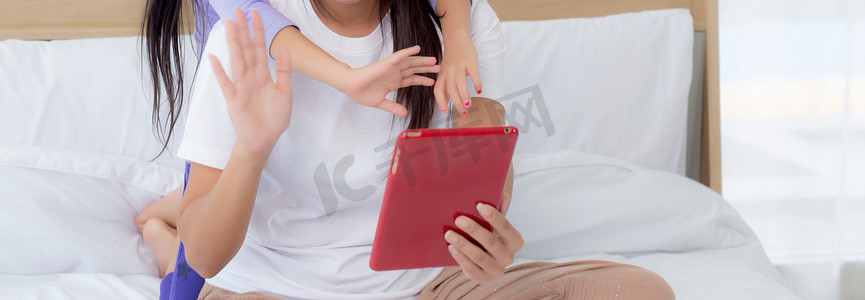 年轻的亚洲母女在平板电脑上视频通话，与家人一起问候，快乐的母亲和女孩利用技术与互联网进行在线交流，两个人。