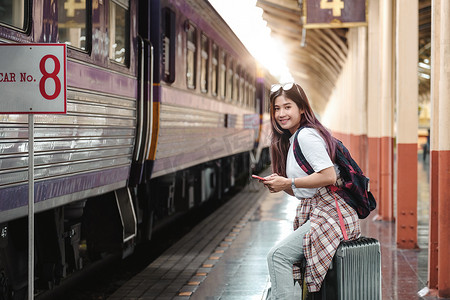 肖像吸引力亚洲女游客坐在火车站带着行李。