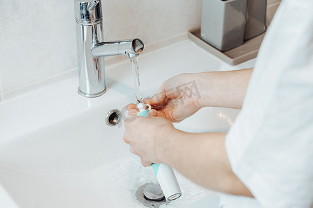 一位女士刷完牙后用水清洗他的电动牙刷件