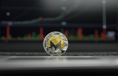 门罗币摄影照片_银色笔记本电脑黑色键盘上的门罗币金币和银币以及屏幕上的图表图表作为背景。