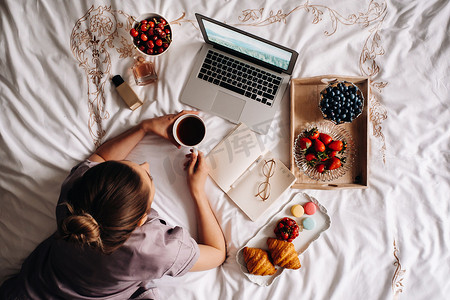 一个女孩晚上坐在床上，手里拿着智能手机吃着草莓，一个女孩在床上睡前吃糖果。
