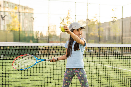 健身的小女孩摄影照片_试图在室外球场打网球的小女孩