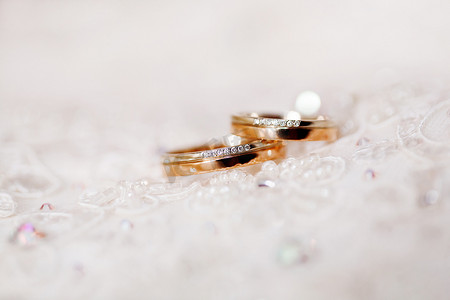 镶有钻石的金色结婚戒指躺在蕾丝丝绸织物上。