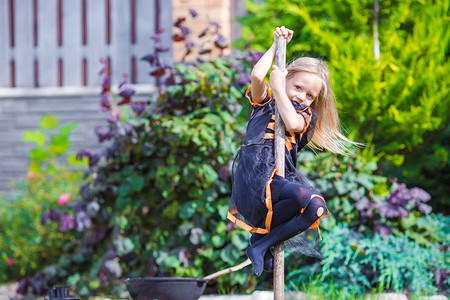 蜘蛛开心摄影照片_穿着万圣节服装的可爱小女孩在扫帚上玩得很开心。