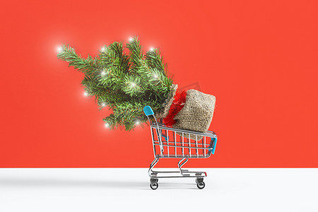 圣诞树装饰着圣诞灯，购物车来自一家以红色背景隔离的超市。