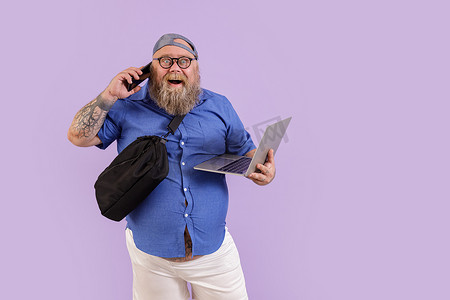 有趣的胖男性，带着笔记本电脑和斜挎包，在紫色背景的电话中交谈