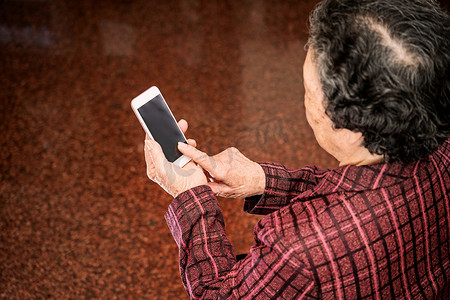 机上老人摄影照片_亚洲老妇人坐着看现代智能手机上的东西，与家里的其他人建立联系，生活技术，特写