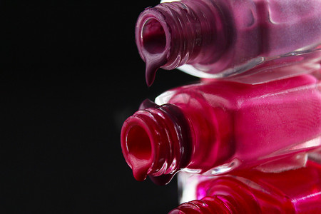倒油瓶摄影照片_美容背景保护指甲油从罐装紫色红色勃艮第粉红色的小瓶中倒出，从侧面特写