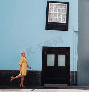 一位身穿黄色夏装的金发女子站在特内里费岛拉古纳老城的街道上。西班牙，加那利群岛