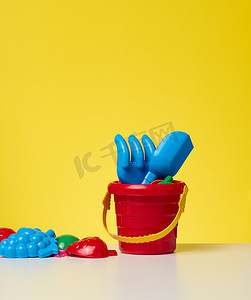 黄色背景中带铲子和玩具的婴儿红色塑料桶
