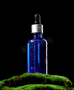 带吸管的蓝色玻璃瓶站在绿色的苔藓上，黑色背景。