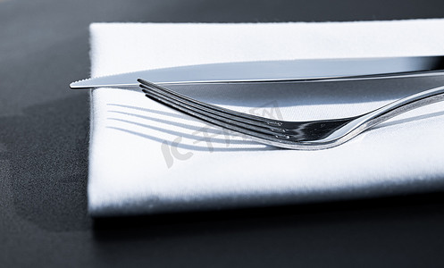 精美菜单摄影照片_户外豪华餐厅的桌上放着白色餐巾的叉子和刀子，婚礼或活动的精美菜单以及餐饮服务理念