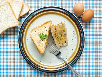 鸡蛋三明治，配料鸡蛋，盐，胡椒和面包放在白盘上，用叉子吃，蓝色背景，用作壁纸