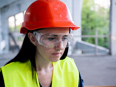 戴防护头盔和护目镜的女建筑师在建筑工地新项目的个人电脑上工作