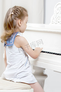 弹奏摄影照片_美丽的小女孩正在一架白色三角钢琴上弹奏。