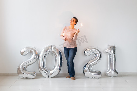 新年庆祝活动和派对理念 — 快乐的年轻女人，在白色背景的 2021 年银色气球附近放着火花。