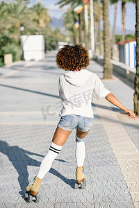 穿着旱冰鞋的黑人妇女在棕榈树的海滨长廊溜旱冰
