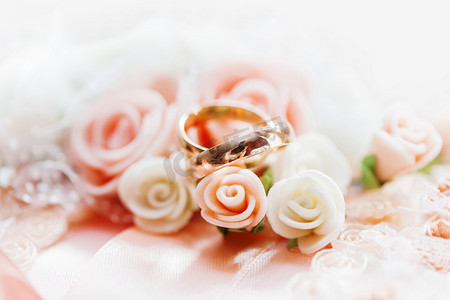 金色婚礼装饰摄影照片_一对金色结婚戒指，在蕾丝面料上，配有玫瑰和蝴蝶结。
