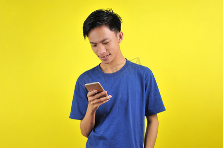 高兴摄影照片_年轻帅气的亚洲男子用智能手机微笑，很高兴