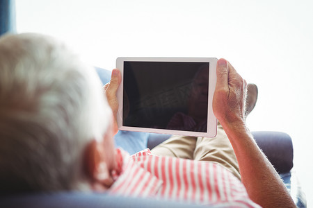 老人摄影照片_躺在沙发上的老人看着数字平板电脑