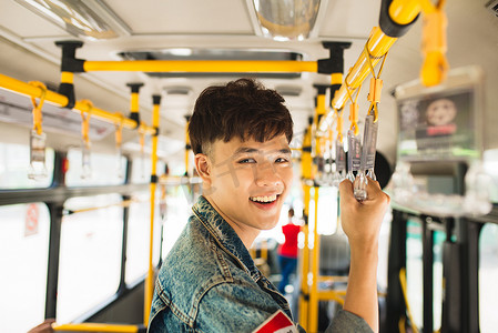 公共生活摄影照片_亚洲男子乘坐公共交通工具，站在公共汽车内。
