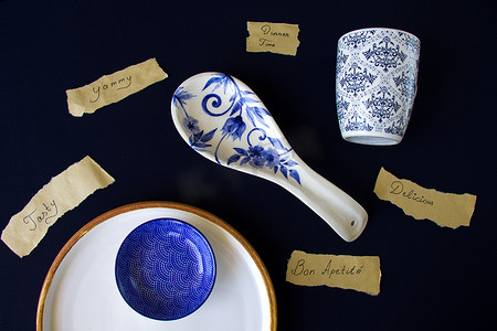 美味，美味，晚餐时间字母和文字，空蓝色餐具，蓝色桌子上的碗和盘子。