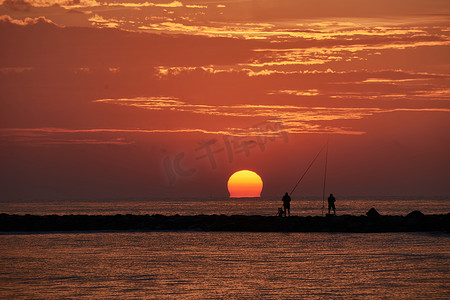 太阳出现在防波堤上的渔民中间