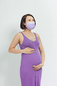 年轻孕妇母亲戴着冠状病毒疾病防护面罩，脸上挂着快乐而冷静的微笑。