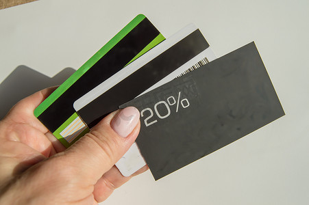 一个男人的手拿着一张打折 20% 的打折卡，还有一张地方的复印件和几张塑料银行卡，储蓄财务的概念