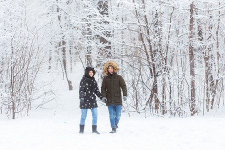相爱的年轻夫妇在白雪皑皑的森林里散步。