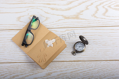 纸蝴蝶摄影照片_空白的笔记本、纸蝴蝶、纸人、太阳镜和怀表